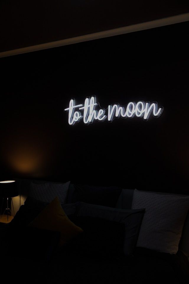 there is a neon sign that says to the moon on the wall next to a bed