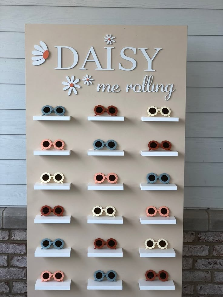 a sign that says daisy me rolling with many pairs of sunglasses on display in front of a brick wall