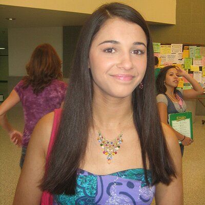 a girl in a purple and blue dress is smiling at the camera with other people behind her