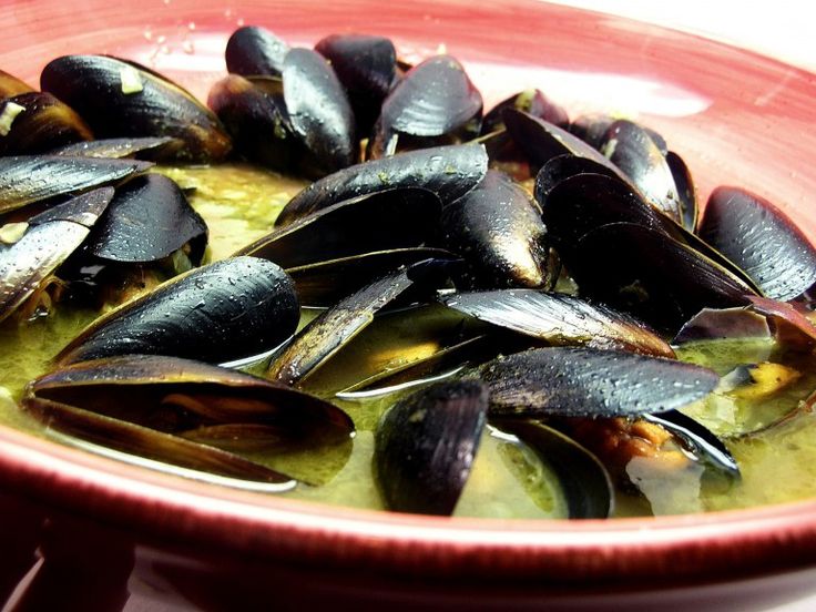 a bowl filled with mussels and broth in a green sauce on top of a table