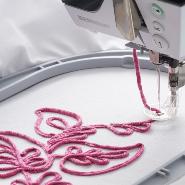 a close up of a sewing machine with pink thread on it's side and an embroidered object in the background