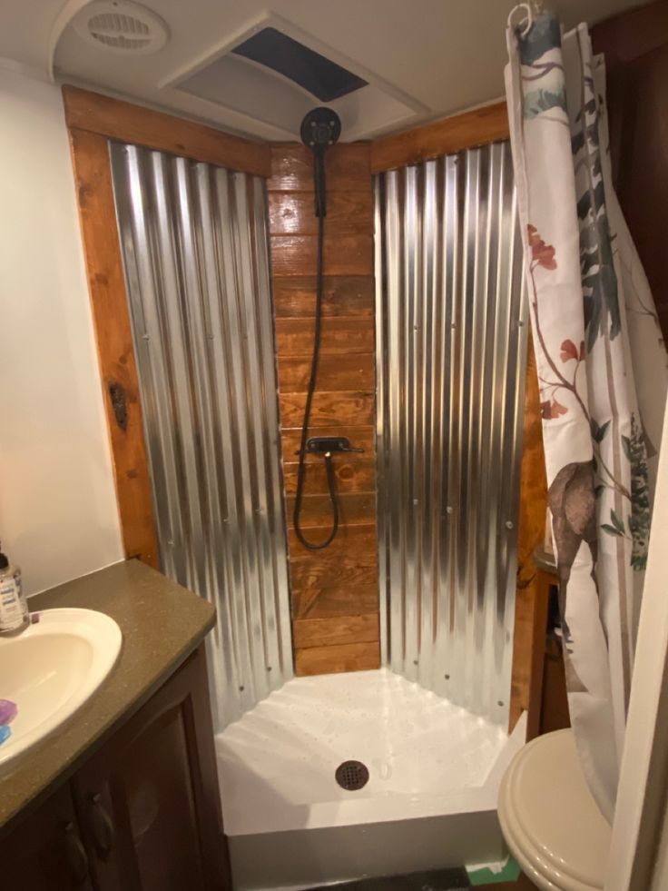 a bathroom with a shower, toilet and sink in it's stall area that has metal slats on the walls