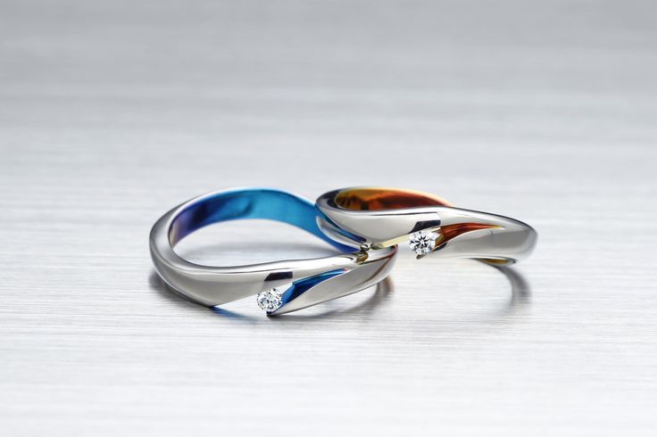 two rings with different colors and sizes on them sitting on a white surface, one has a diamond in the middle