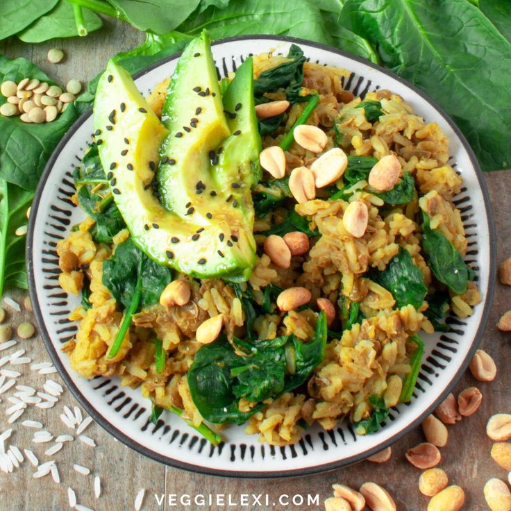 a white plate topped with rice, spinach and avocado wedges next to green leaves