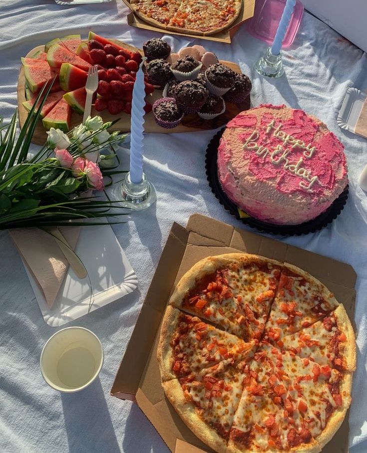 a table topped with pizzas and cakes on top of a white tablecloth covered table