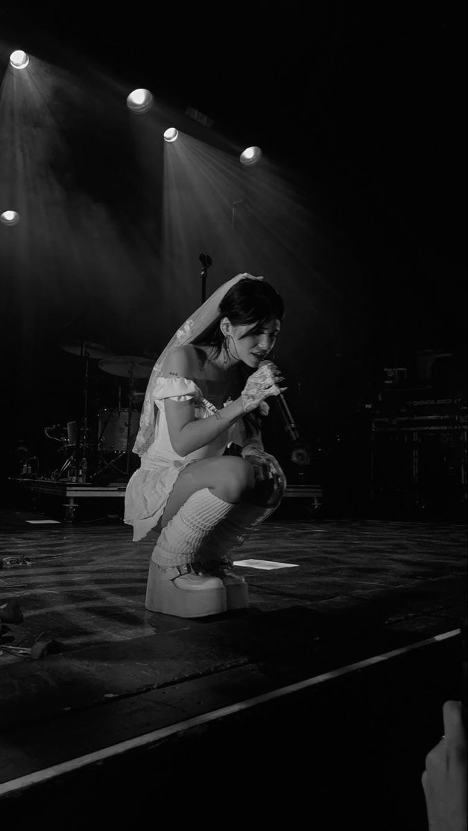 a black and white photo of a woman kneeling on a stool in front of spotlights