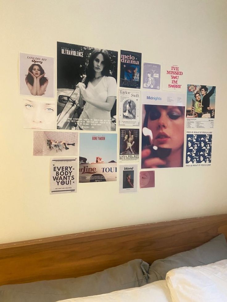 a bed with a wooden headboard and white sheets on top of it next to a wall covered in posters