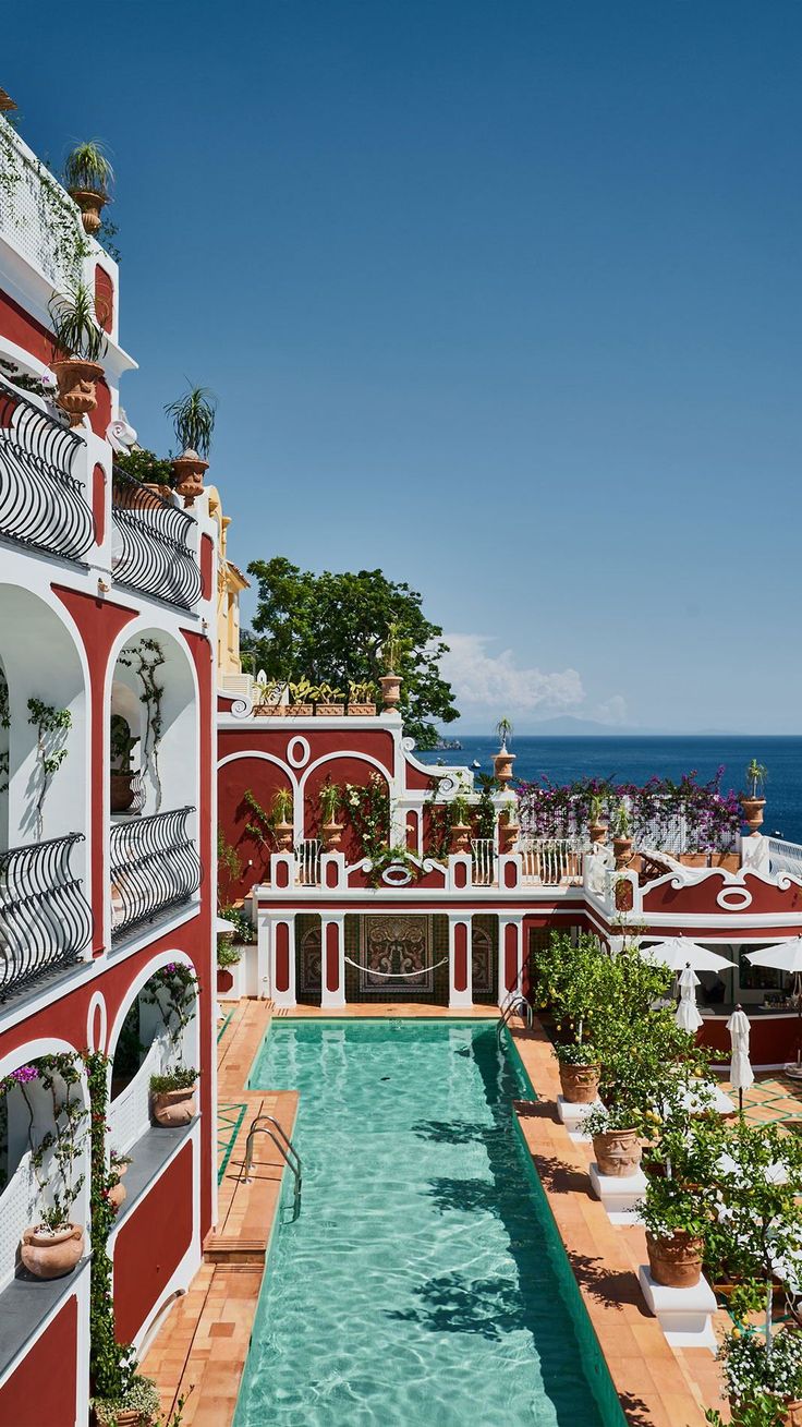 an outdoor swimming pool surrounded by potted plants next to the ocean in front of a red and white building