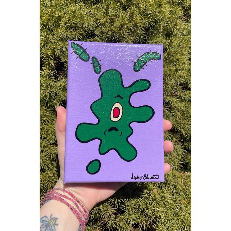 a hand holding up a purple box with an image of a green creature on it