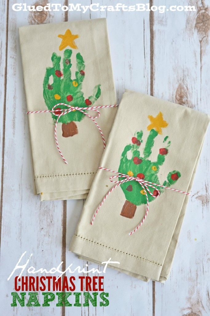 two handprinted christmas tree napkins on top of a wooden table