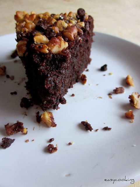 a piece of chocolate cake on a white plate with walnuts around the edges and one slice missing