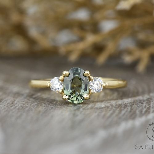 a green and white diamond ring sitting on top of a wooden table