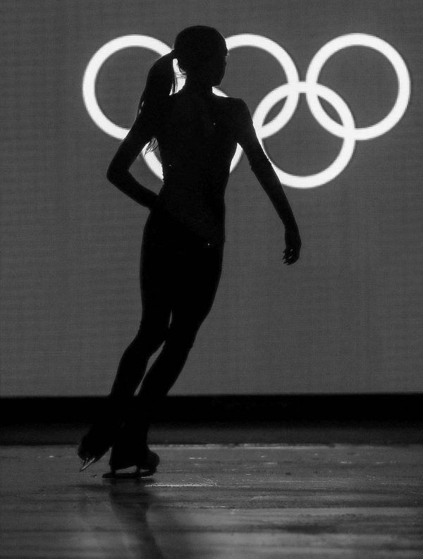 the silhouette of a woman standing in front of a wall with olympic rings on it