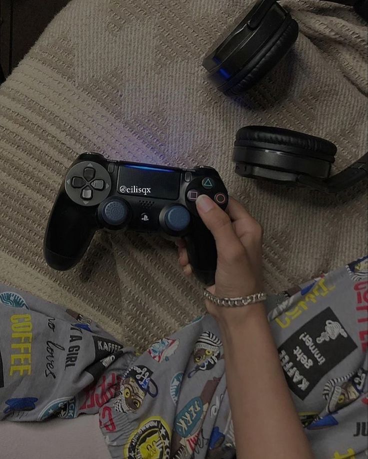 a person holding a video game controller on top of a bed next to headphones