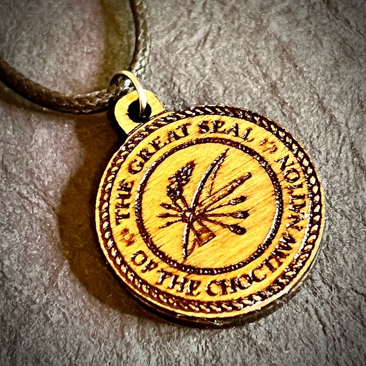 a wooden pendant with the words great seal and arrows in it on a leather cord