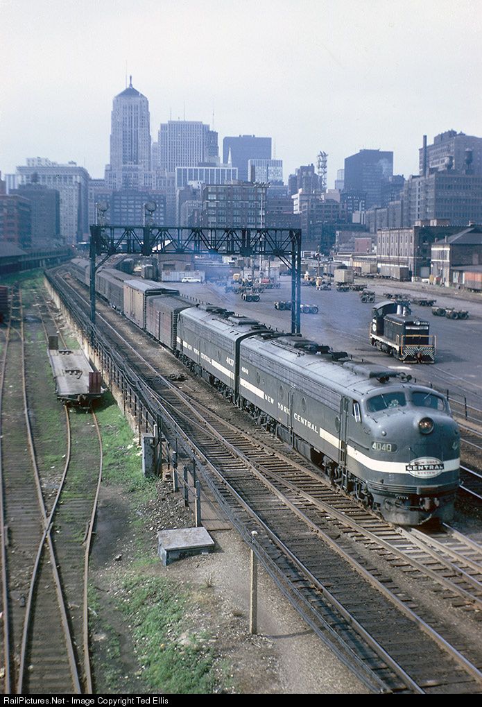 two trains traveling down tracks next to each other in front of tall buildings and skyscrapers