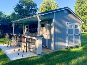 an outdoor bar with chairs in the grass next to a shed that has doors open