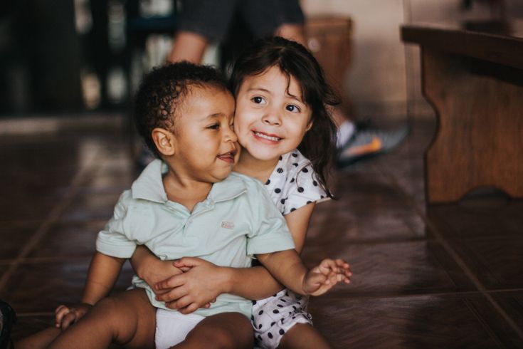 two young children sitting on the floor hugging each other