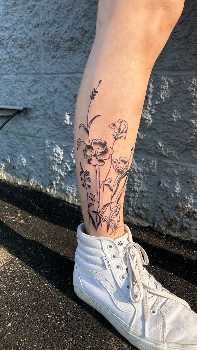 a woman's legs with flowers on them and a white shoe in front of a wall