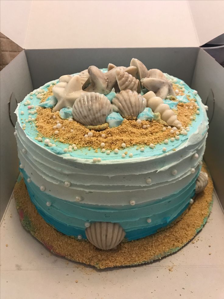 a cake with blue frosting and seashells on top is in a box