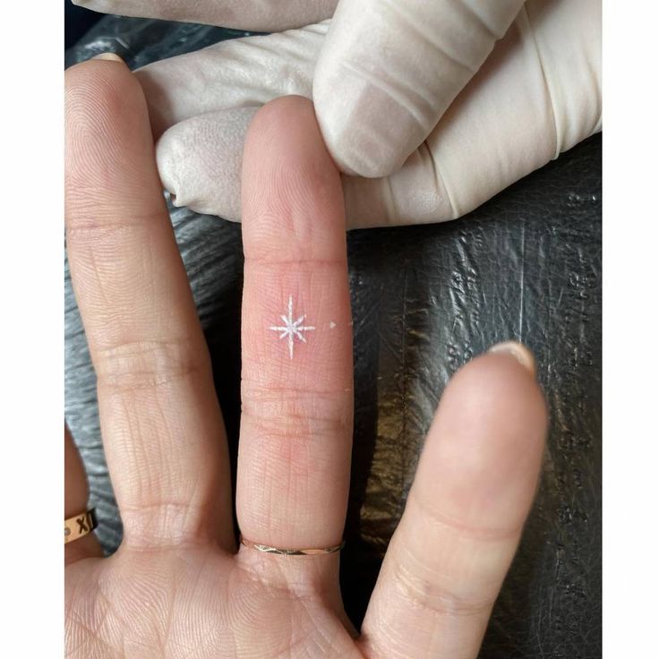 a person's hand with a tiny star tattoo on it, next to gloves