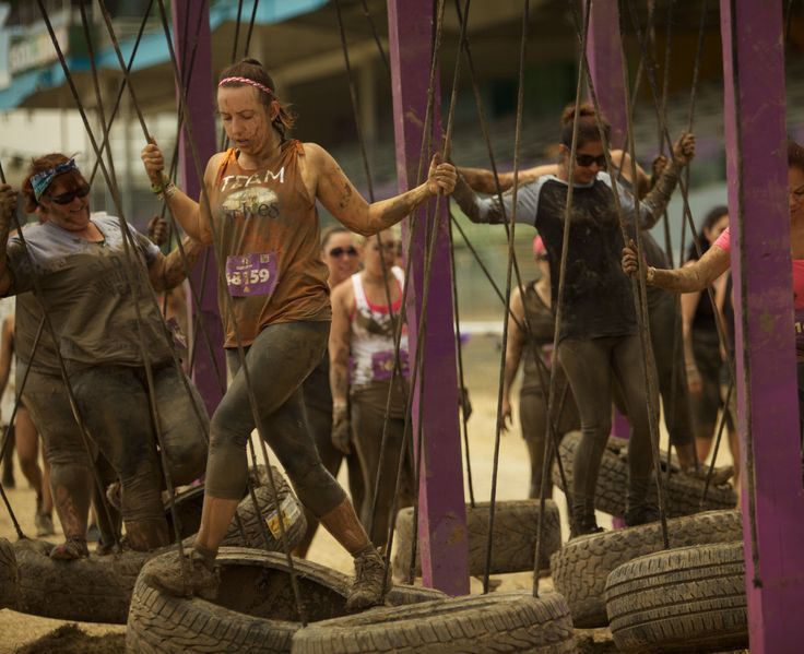 a group of people climbing on old tires in the dirt with one person holding onto them