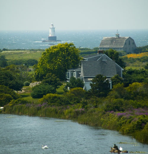 two people are in the water near some houses and a light house with a lighthouse in the background