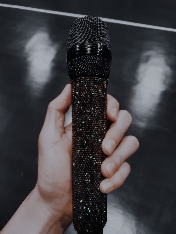 a hand holding a microphone in front of a black and white photo with sparkles