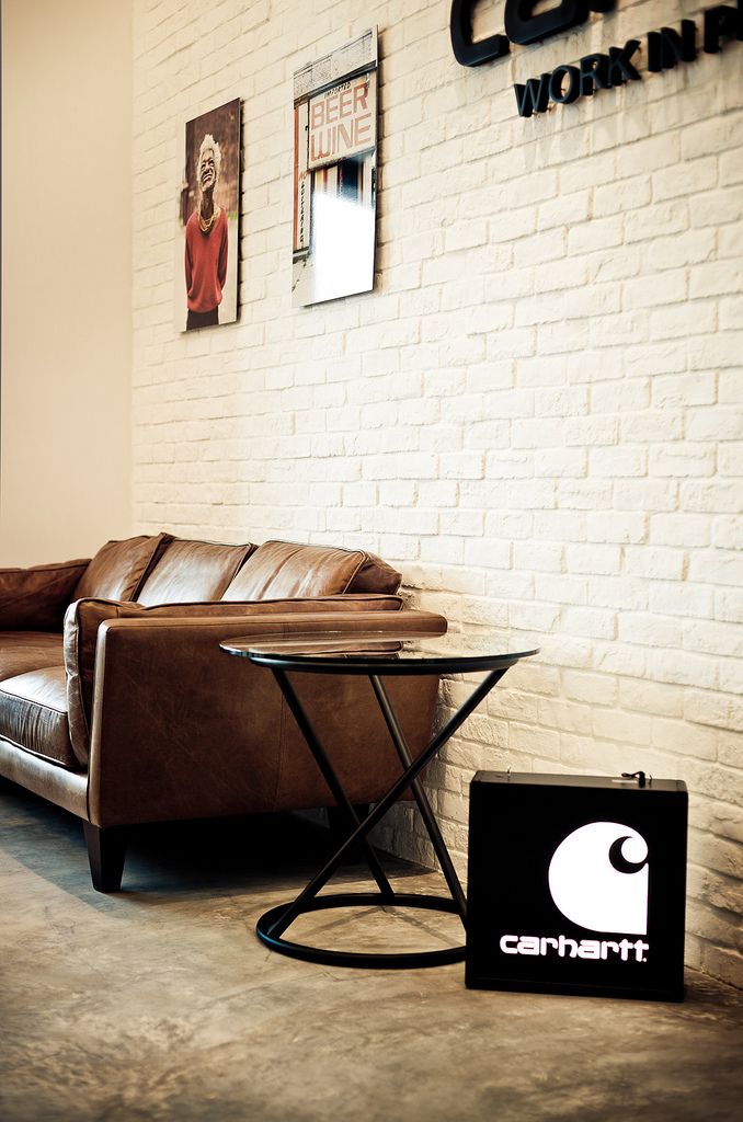 a brown leather couch sitting in front of a white brick wall next to a coffee table