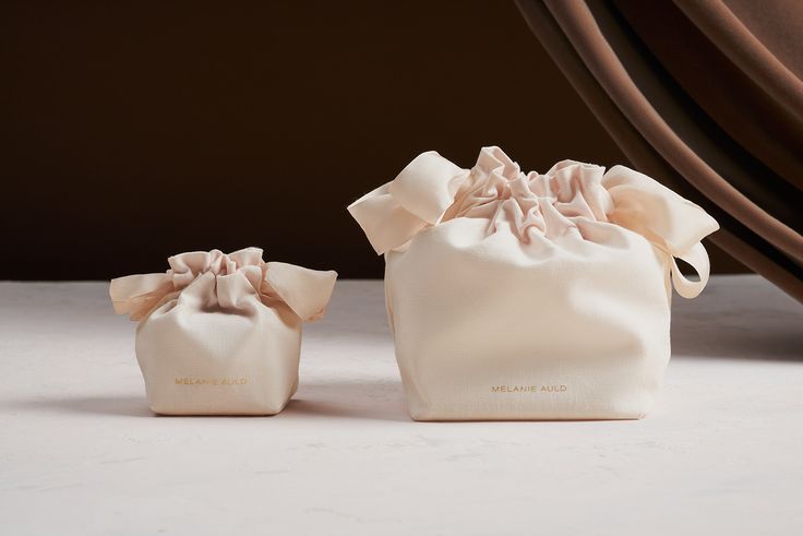 two small bags with bows on them sitting in front of a curtain and drapes