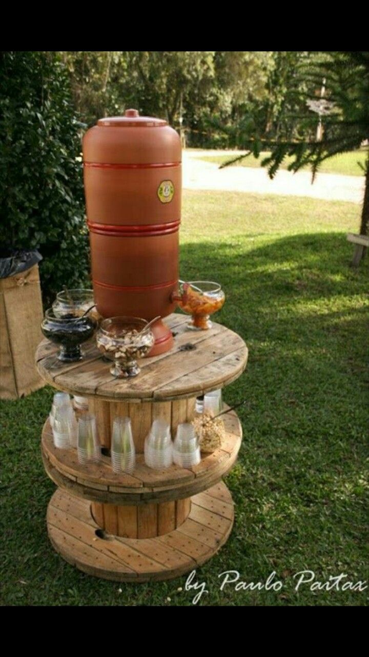 an outdoor table made out of pallet wood with bottles on it and a large barrel in the middle