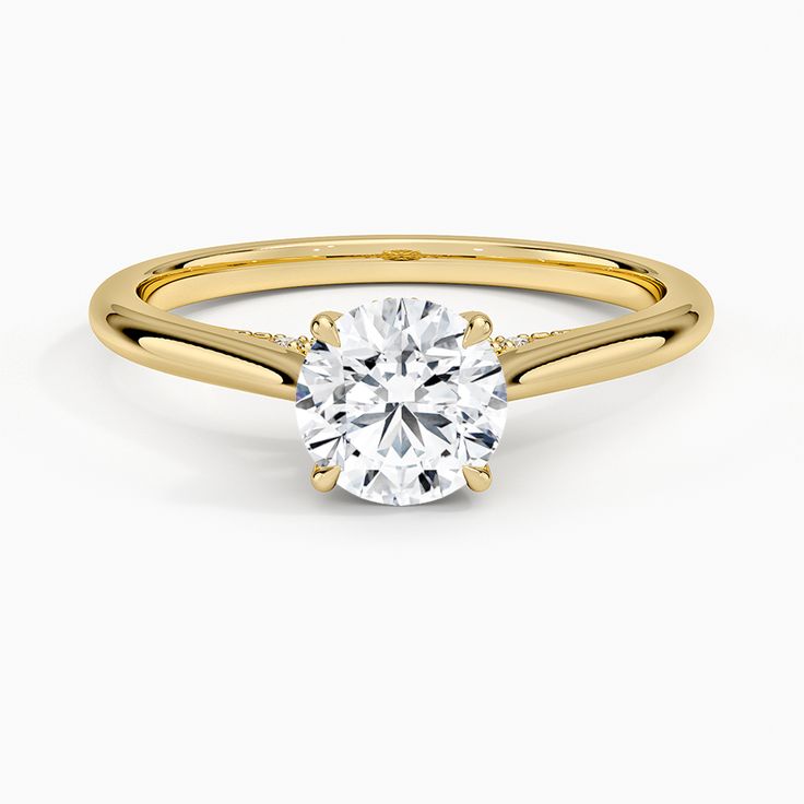 a yellow gold engagement ring with a round cut diamond in the center, on a white background