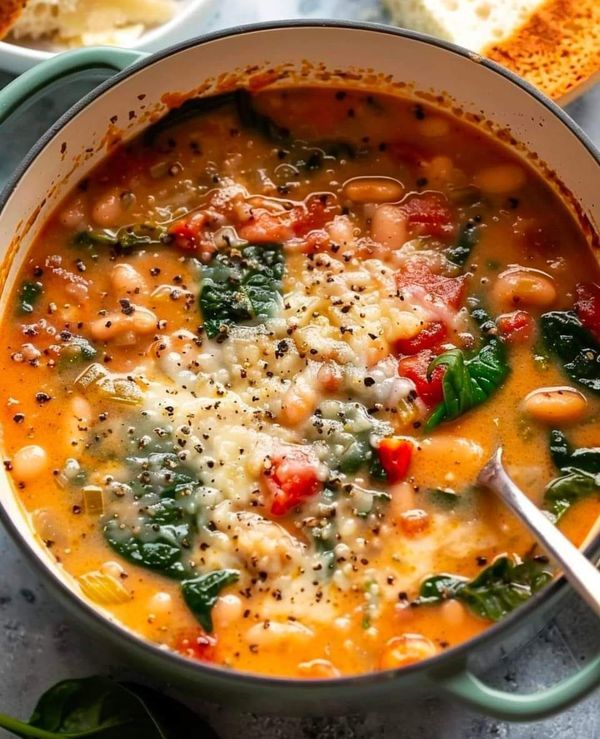 a bowl of soup with spinach, beans and cheese in it next to bread