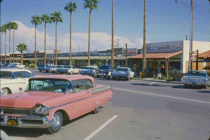 an old pink car parked in front of a gas station with palm trees on the side