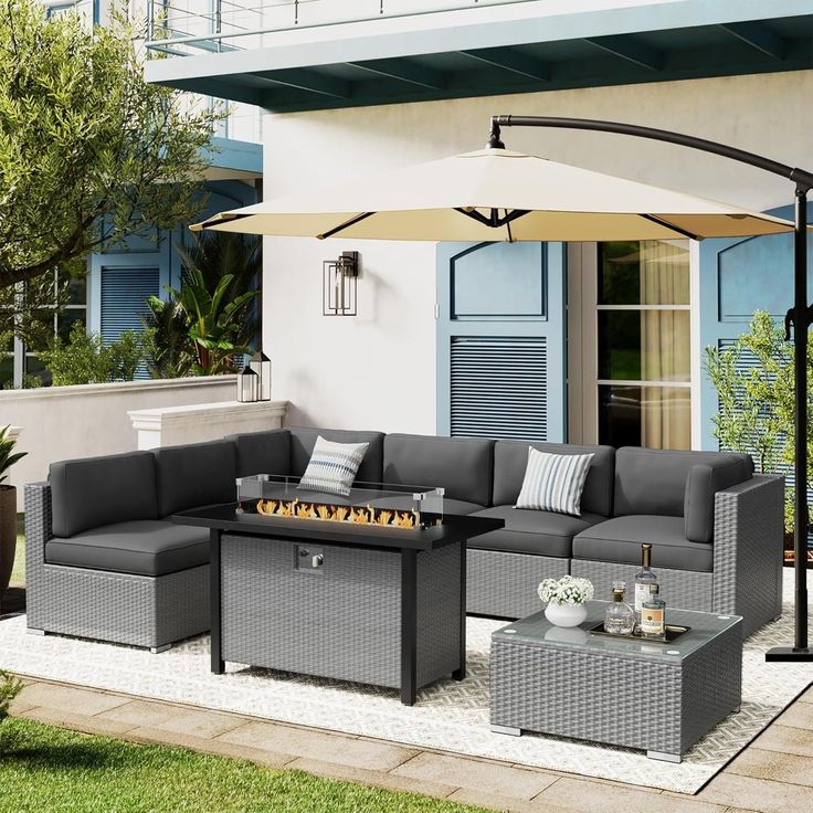 an outdoor living room with grey wicker furniture and white umbrella over the fire pit