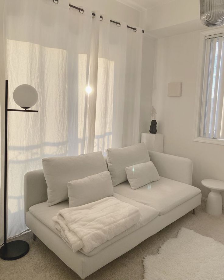 a white couch sitting in the middle of a living room next to a window with curtains