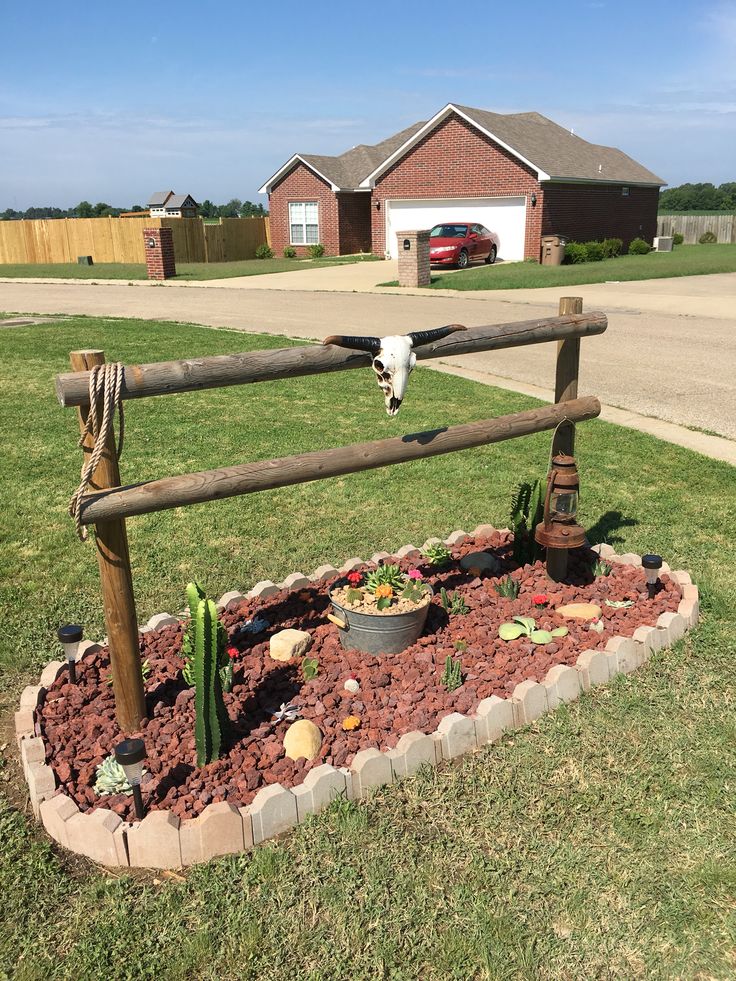 a cow skull is mounted to a wooden fence in a flower bed with cactuses and succulents