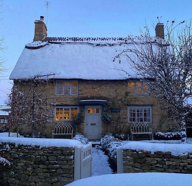 a stone house covered in snow next to a fence and tree with no leaves on it