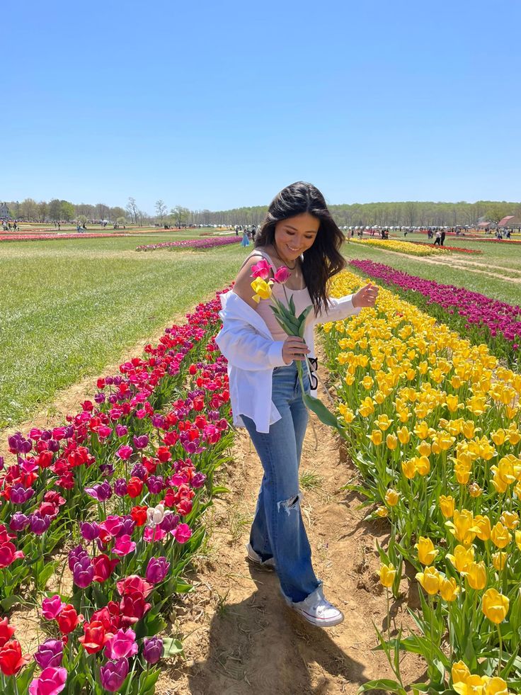 a woman standing in the middle of a field with lots of tulips and other flowers