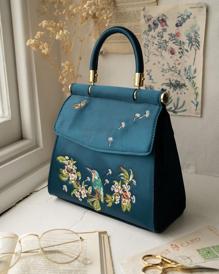 Designed in our hero narrative from our Morning Song collection, our Kingfisher Mini tote in Teal satin is a luxe looking carryall to go with any Spring time outfit. Exquisitely crafted with one of nature’s most fascinating feathered friends, you’ll find you have a new spring in your step every time you carry it. Whether heading out day tripping or for a special occasion, this versatile tote is spacious enough for all your everyday essentials.
 Key Features
  Approx. 20cm L x 18cm H x 6cm W
 Cha Creative Handbags, Fable England, Spring Time Outfits, Morning Songs, Academia Outfits, Dad Jewelry, Luxury Christmas Gifts, Green Gables, Pearl Jewellery Earrings