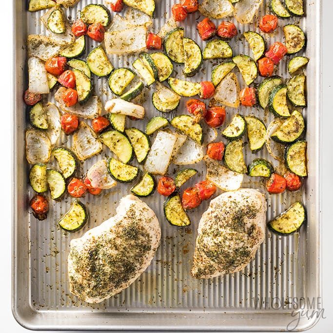 chicken, zucchini and tomatoes on a baking sheet with seasoning sprinkles