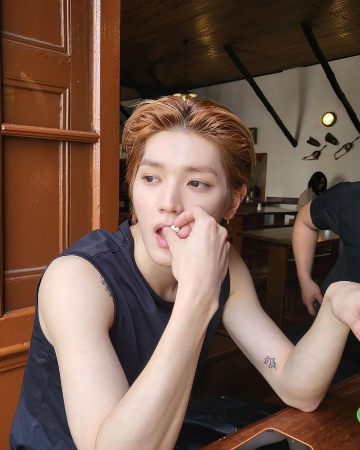 a young man sitting at a table with his hand on his mouth and another person standing behind him