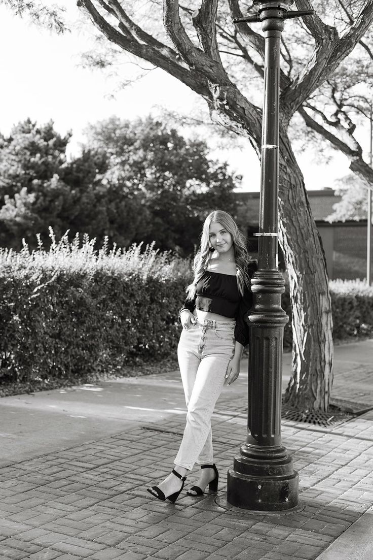 a woman standing next to a lamp post on a sidewalk in front of a tree