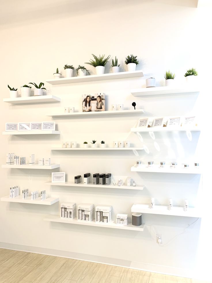 a white wall filled with lots of shelves covered in plants