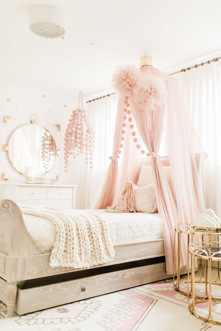 a pink canopy bed in a girls'bedroom with white walls and flooring, along with chandeliers