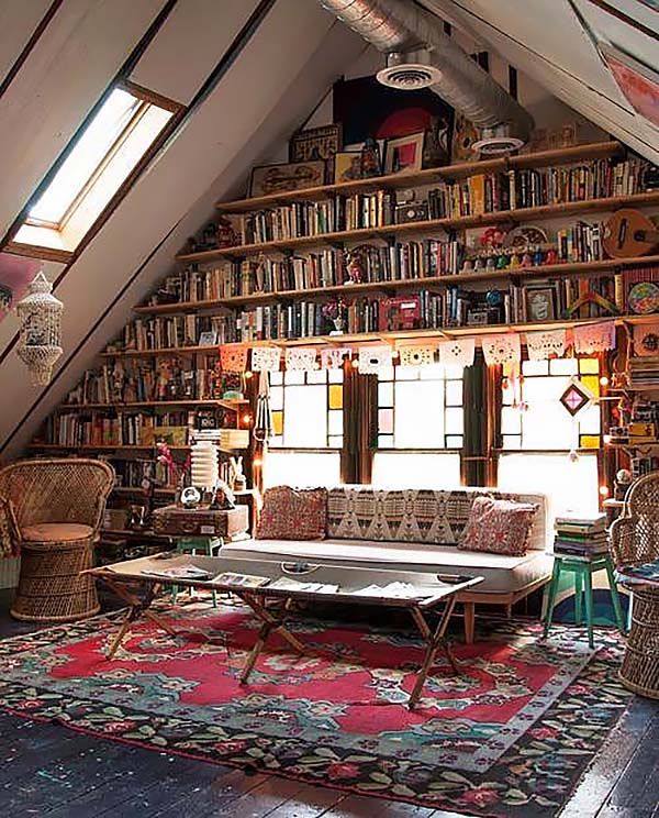 a living room filled with lots of furniture and bookshelves under a slanted ceiling