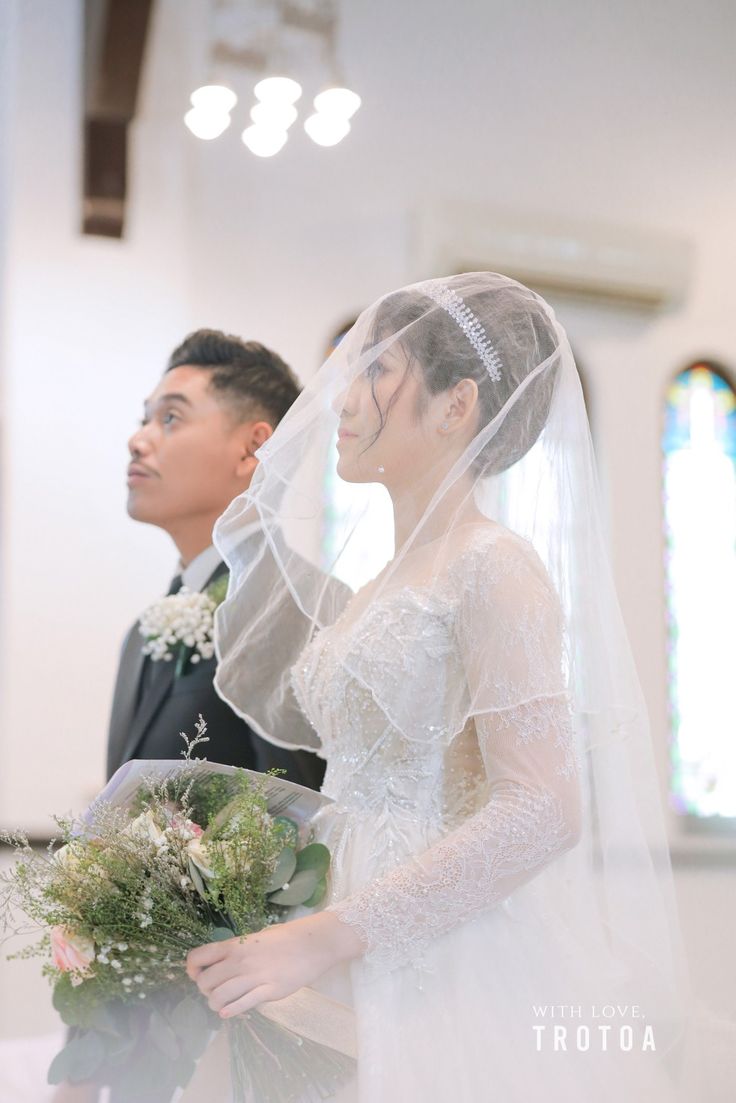 a bride and groom standing in front of the alter at their wedding ceremony, with veil draped over their heads