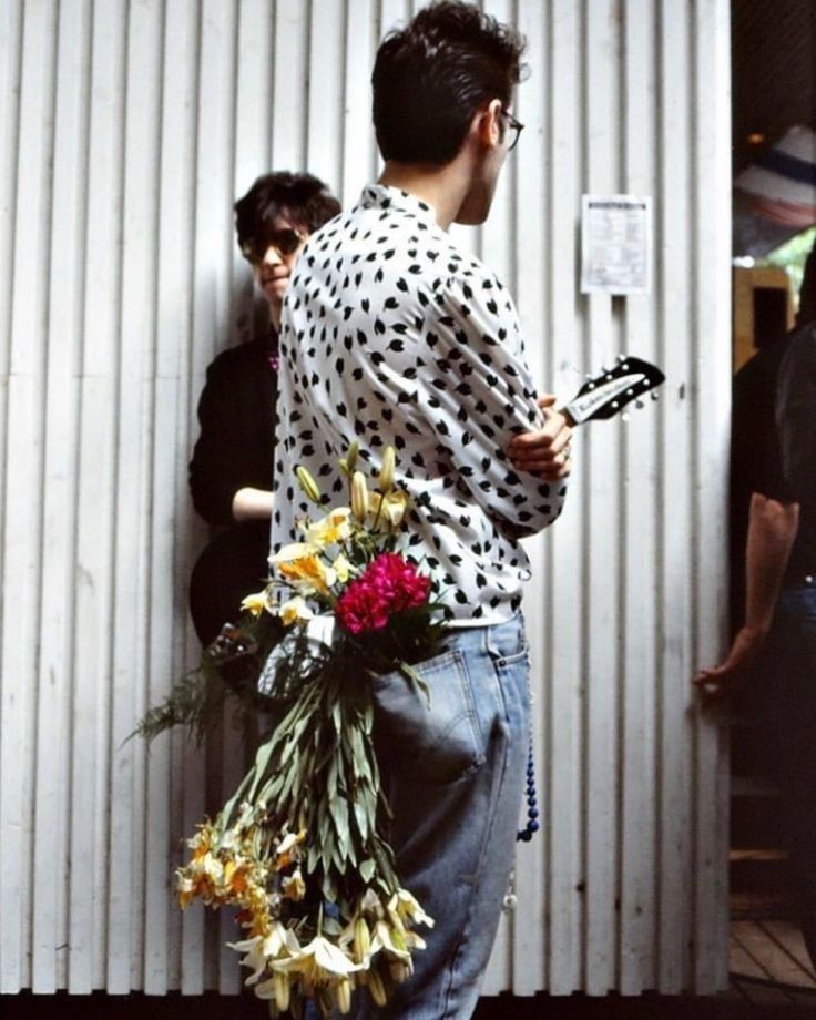 a man standing next to a building holding flowers