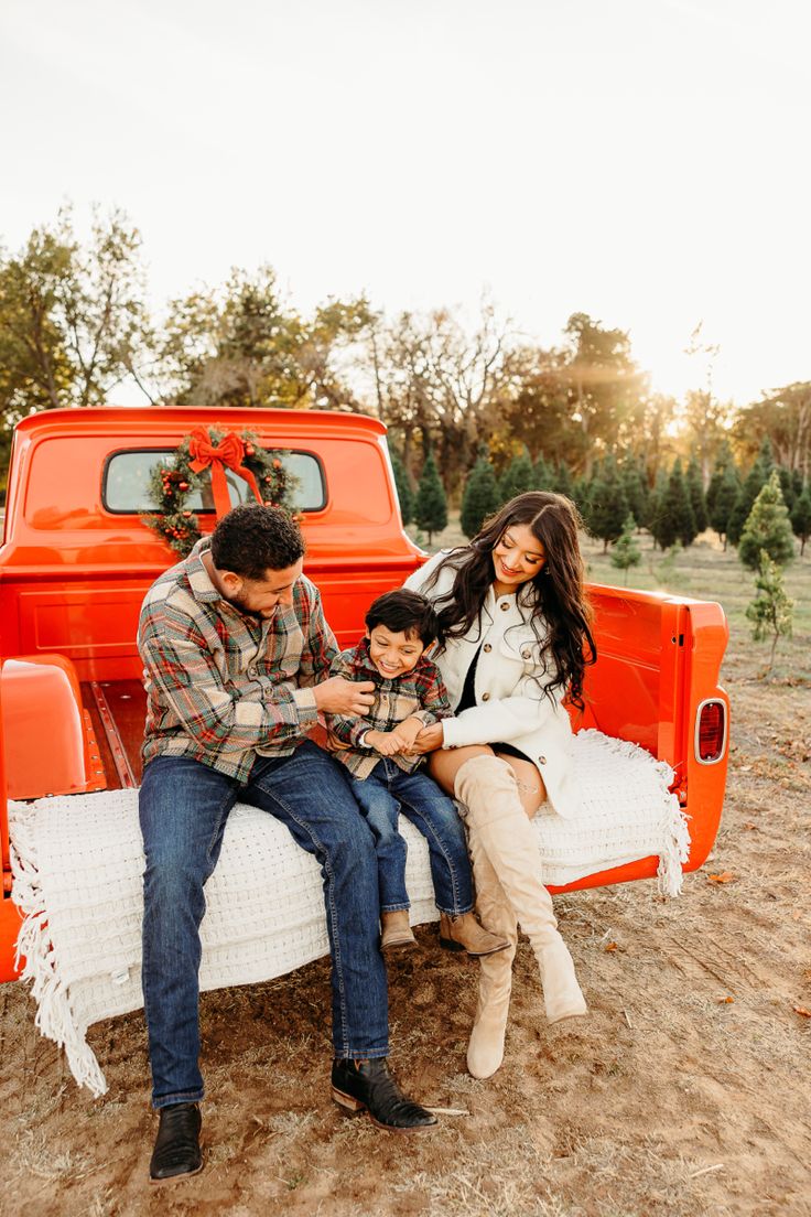 a man and woman sit on an orange truck with their son, who is sitting on the bed