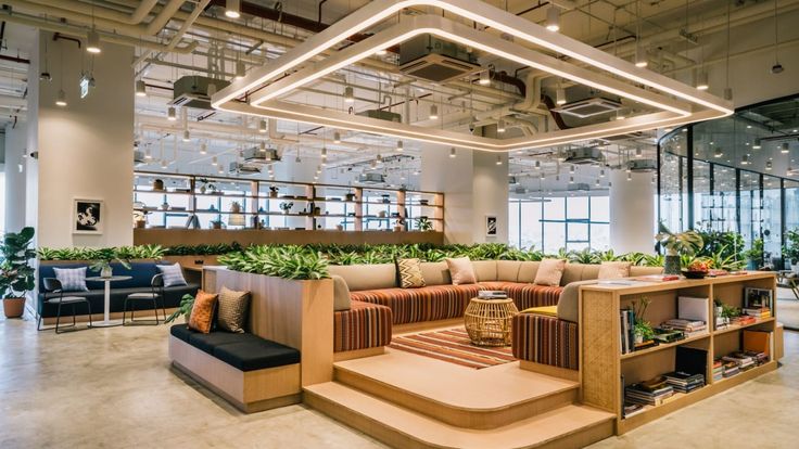 an office lobby with couches, tables and plants on the wall in front of windows